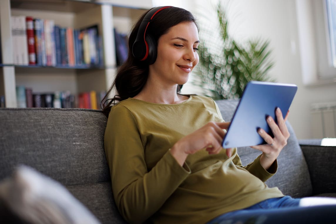 Woman uses tablet and wears headphones as she streams internet at home.