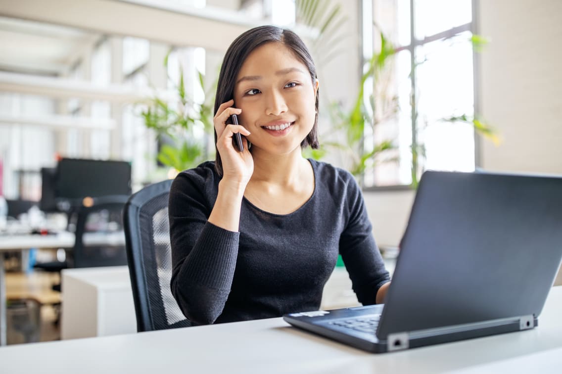 Woman talks on phone and works on laptop at the same time.